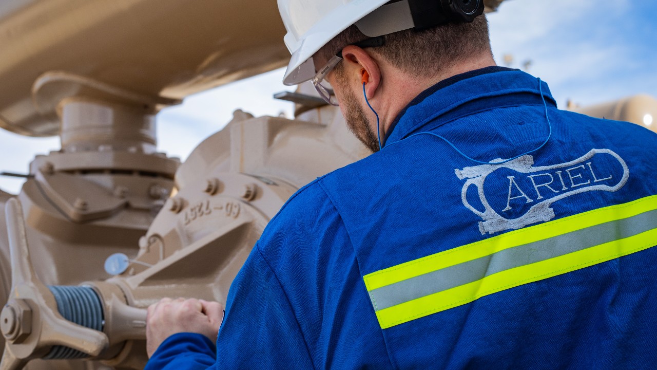 An Ariel logo on the back of an Ariel technician examining a compressor at a compressor station