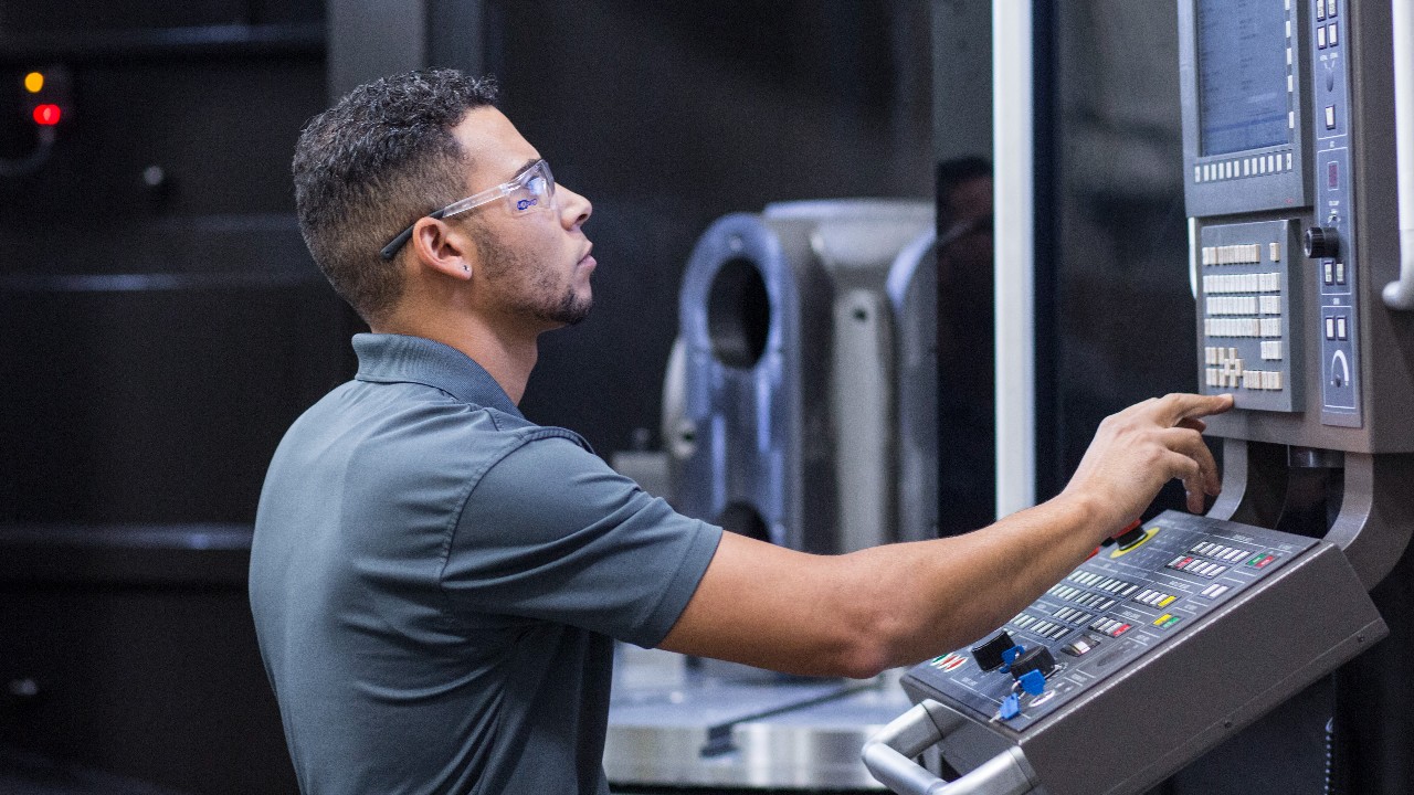 An Ariel machinist working on a cylinder with his hand on a control panel 