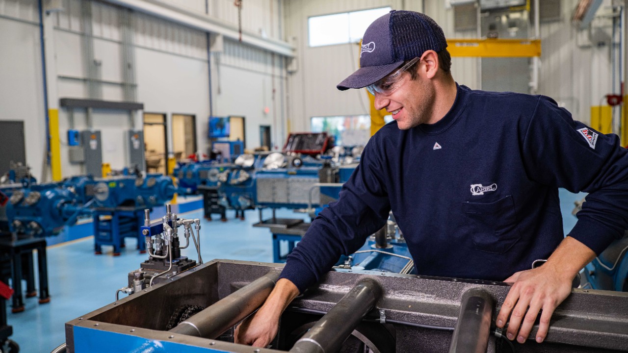 An employee working on the frame of a compressor wearing riel branded clothing