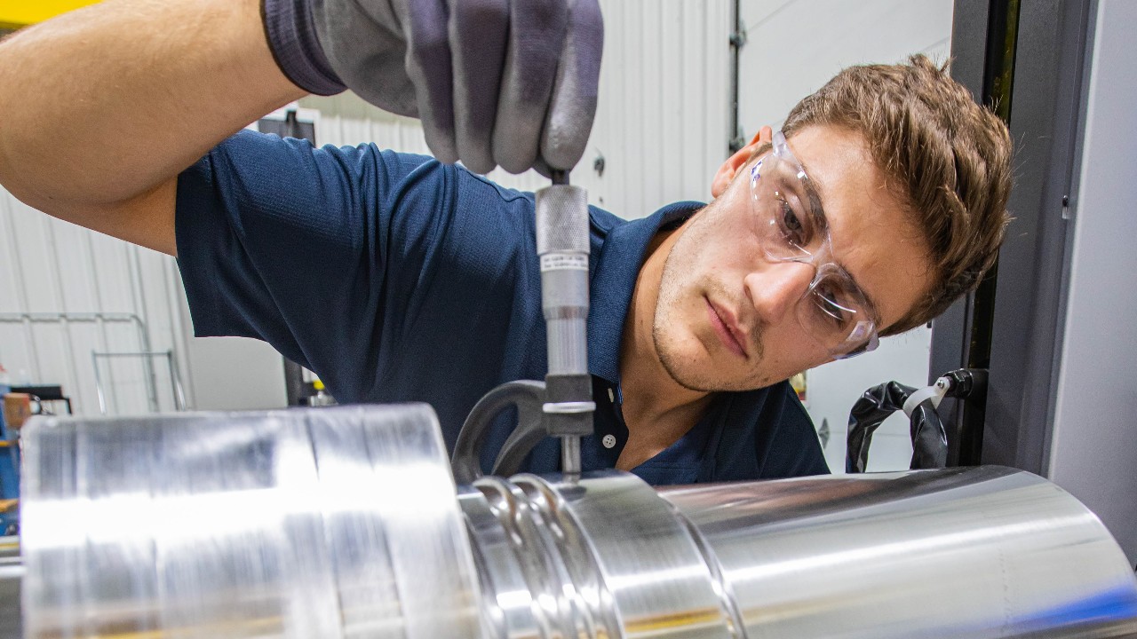 A quality inspector uses a micrometer to ensure a crankshaft is the proper size