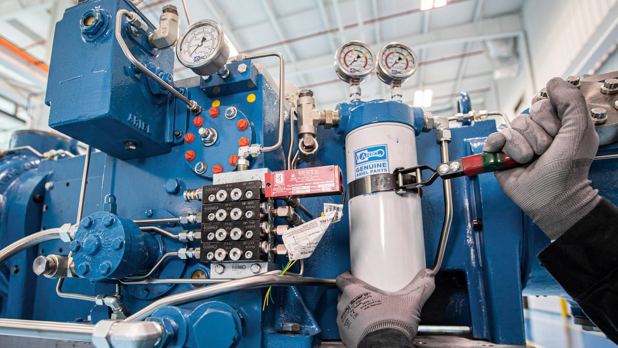 Gloved hands using a tightening tool to attach a spin on oil filter to a small line compressor