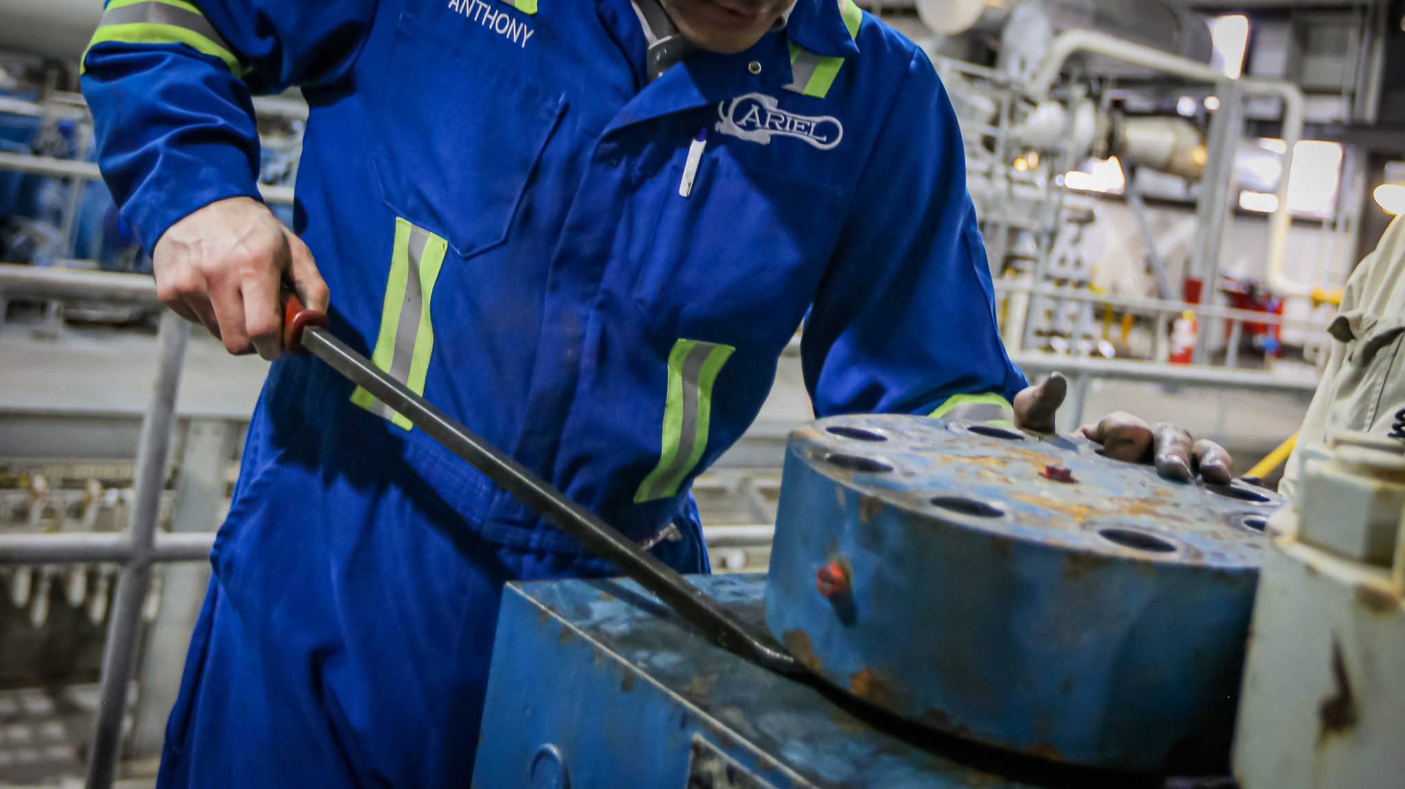 An ariel field technician using a prybar on a high pressure cylinder