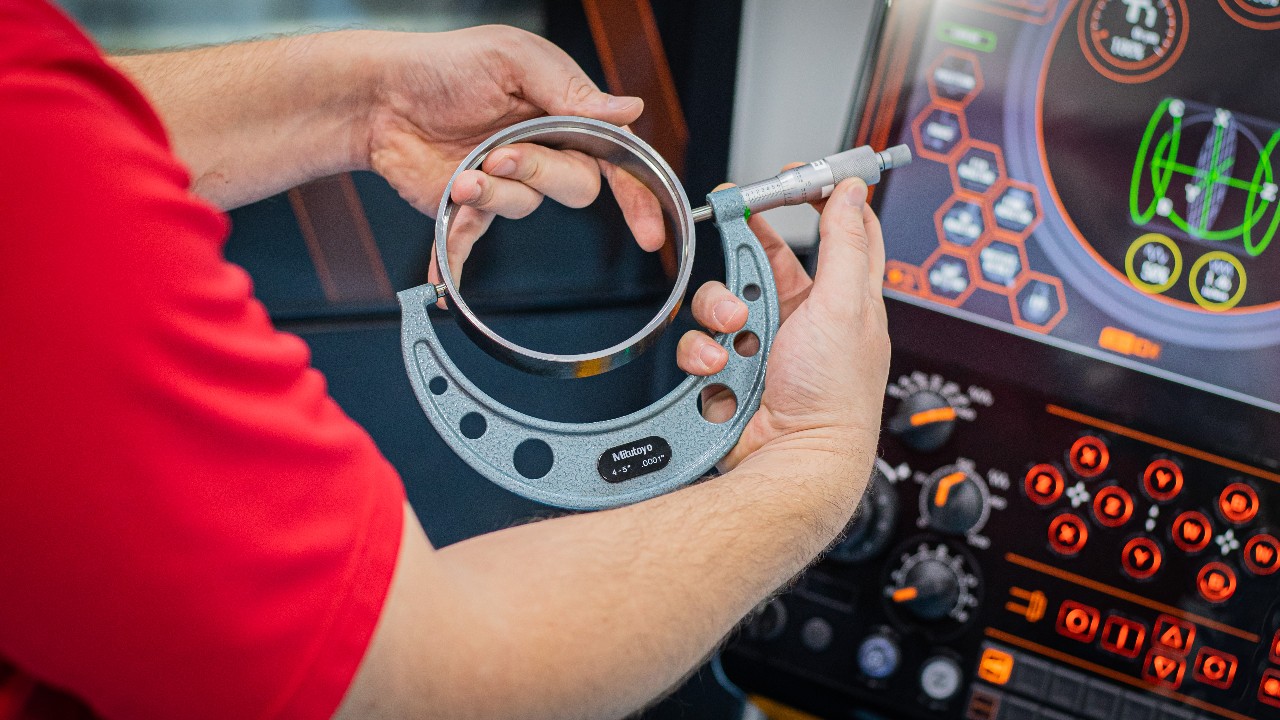 Hands holding  a valve part and taking a measurement with an outside micrometer