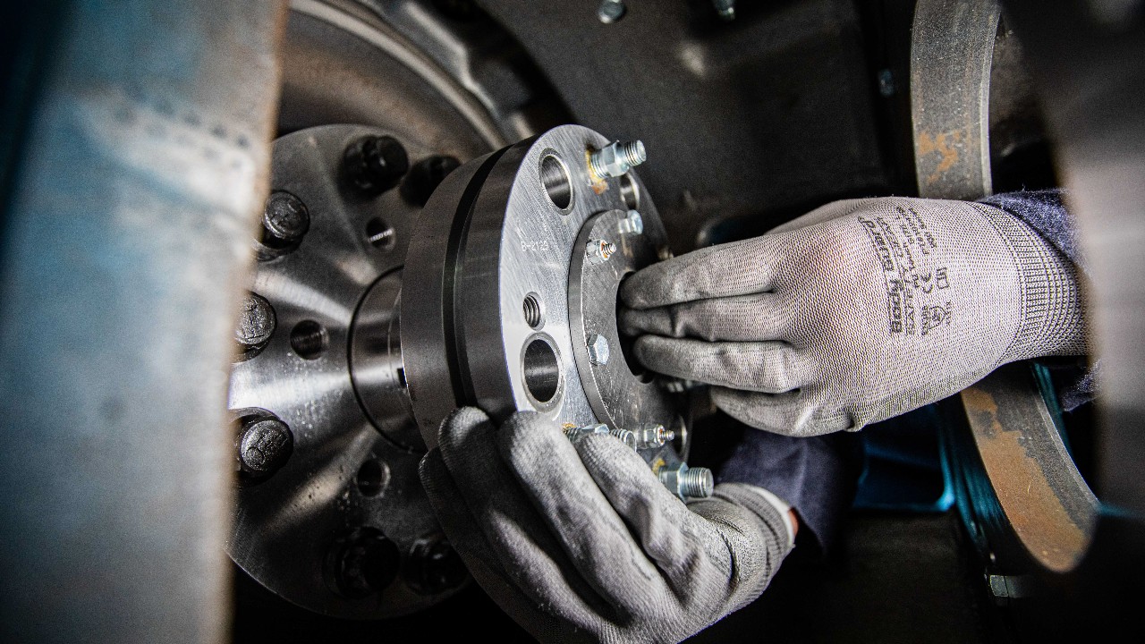 Gloved hands reaching into a guide to install a packing case into an Ariel compressor