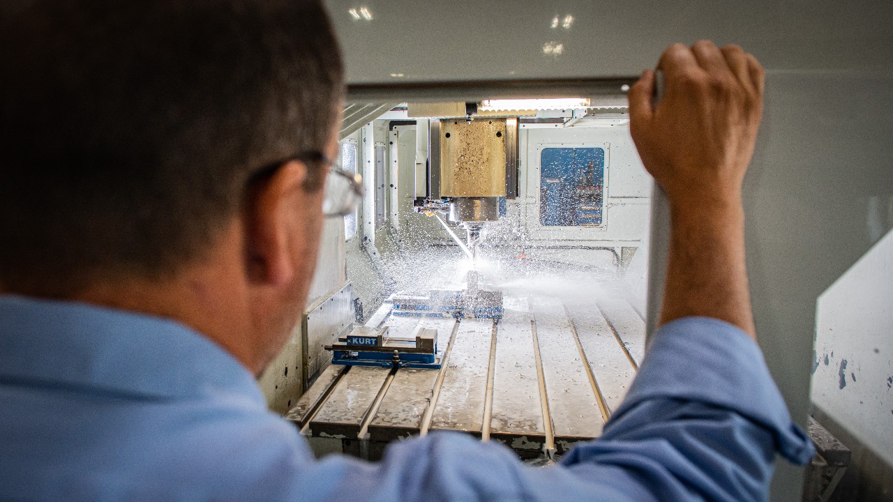 An employee looking into a mill while it sprays coolant and machines an Ariel part