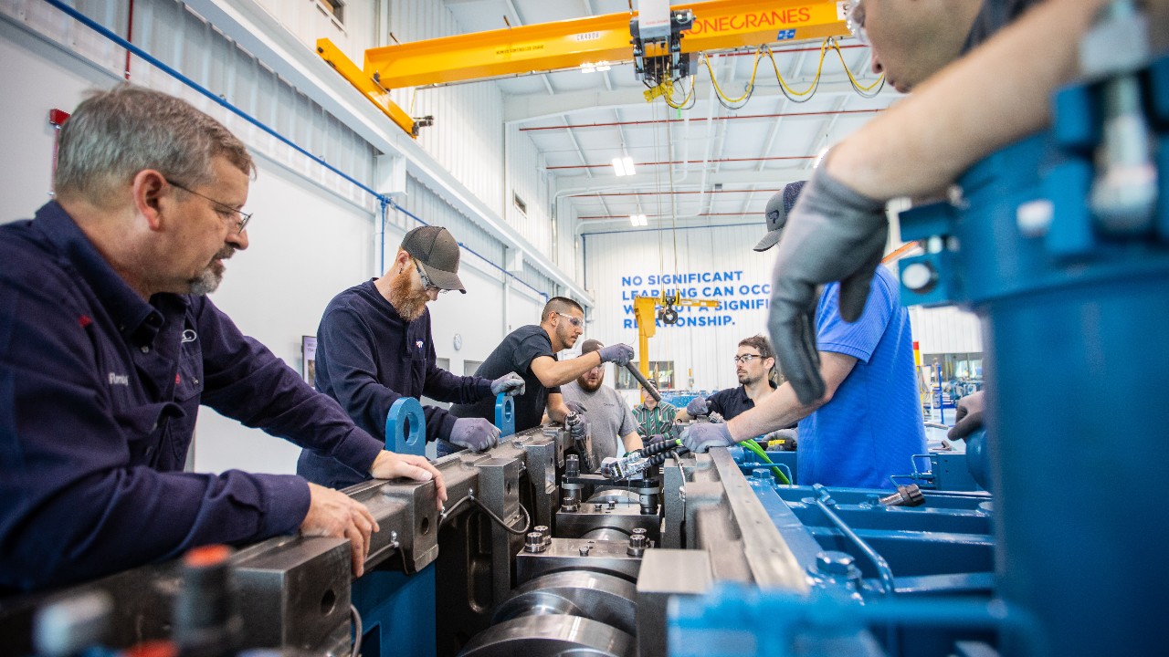 Mechanics and trainers gathered around a large line compressor performing maintenance in a lab