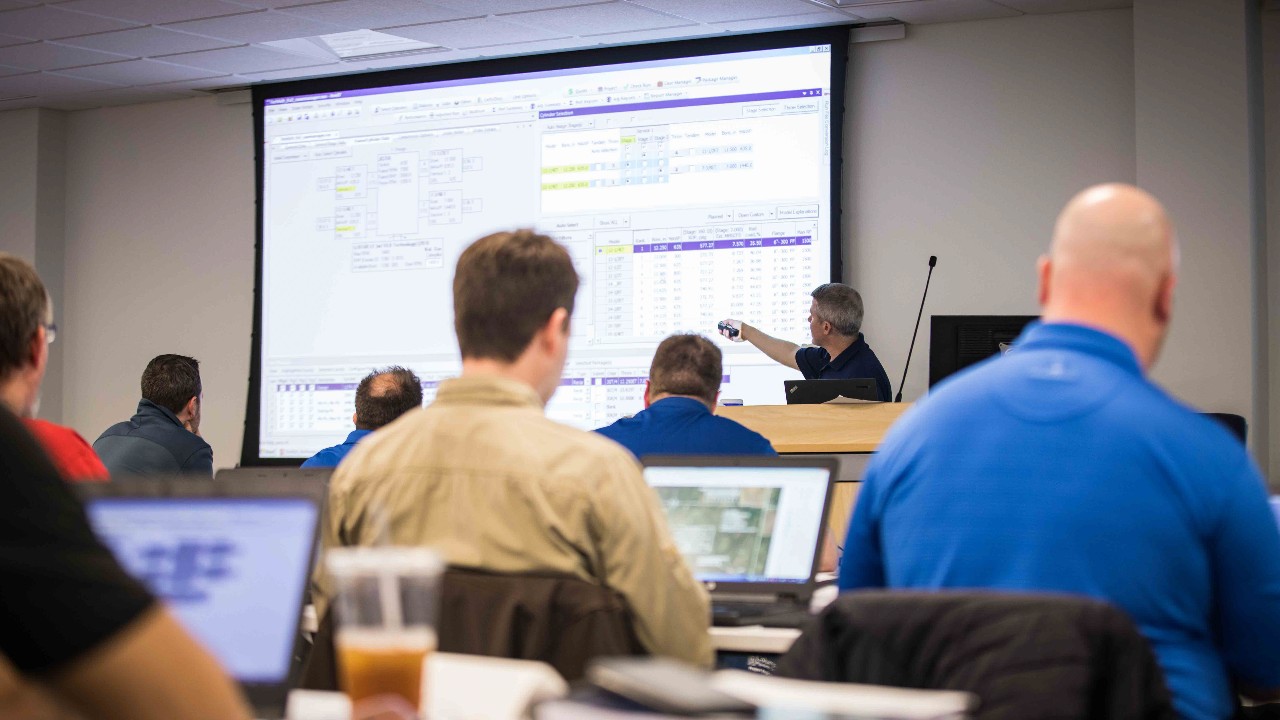 Classroom of mechanics at desks, with computers, watching a presentation